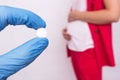 The doctor holds a pill in the form of a complex of vitamins and folic acid on the background of a pregnant girl, lack of vitamins