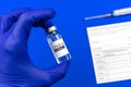 Doctor holds vaccine vial, covid-19 vaccination record card in hospital, blue background