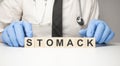 Doctor holds wooden cubes in his hands with text stomack