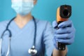 Doctor with infrared thermometer on blue background, closeup. Checking temperature during Covid-19 pandemic Royalty Free Stock Photo