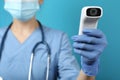 Doctor with infrared thermometer on blue background, closeup. Checking temperature during Covid-19 pandemic Royalty Free Stock Photo