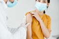 doctor injecting a woman in a yellow t-shirt in the shoulder close-up covid vaccination Royalty Free Stock Photo