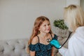 Doctor inspecting by stethoscope a girl in the grey room. Focus is at the girl