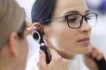 Doctor laryngologist examining ear of female patient with glasses using otoscope