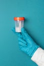 Doctor in latex gloves holds a plastic container with semen or saliva samples on a blue background. Medical concept Royalty Free Stock Photo