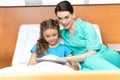 Doctor and little girl using digital tablet and sitting on bed Royalty Free Stock Photo