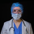 The doctor looks scared in protective glasses and a medical mask, black background. Nurse with open eyes, close-up portrait Royalty Free Stock Photo