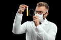 Doctor looks at a test tube with liquid through a magnifying glass, loupe, is isolated on a black background. Scientific research