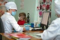 Doctor makes notes on card of little patient after examination, recording appointment and results. Masked woman and boy