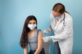 Doctor making injection of coronavirus vaccine to Indian teenage girl in face mask on blue studio background Royalty Free Stock Photo