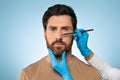 Doctor making marks on male face, handsome caucasian man on consultation at surgeon, standing on blue background Royalty Free Stock Photo