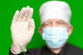 Doctor male in surgical face mask on defocus foreground put forward palm of his hand in protective latex glove