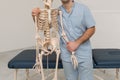 Doctor man pointing on arm of human skeleton anatomical model. Physiotherapist explaining joints model. Chiropractor or