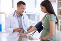 Doctor, man and pregnant woman in clinic for blood pressure, healthcare checkup and consultation. Male medical expert Royalty Free Stock Photo