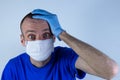 Doctor man in a protective mask on a blue background. Warns laid a hand on his head, indignant at the fear of surprise