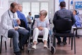 Doctor man sitting in waiting hospital area with senior disability woman Royalty Free Stock Photo