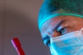 Doctor with mask and cap in his office looking worried to observe a blood sample from an analysis.