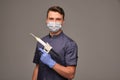 A doctor in a mask on a gray background in gray clothes holds dental treatment tools in his hands Royalty Free Stock Photo