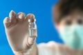 A doctor in a mask and white gloves holds and showing a medicine bottle with vaccine Royalty Free Stock Photo