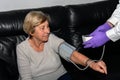 A doctor measures a senior woman`s blood pressure with a blood pressure cuff on her arm while she is sitting on a couch. Concept Royalty Free Stock Photo