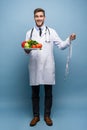 Doctor with a measuring tape and a plate with vegetables and fruit isolated on light blue background. Royalty Free Stock Photo