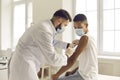 Doctor in face mask giving antiviral vaccine to young patient during vaccination campaign