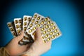 Doctor in medical gloves holds in his hand medicines in a package in yellow capsules on a blue background Royalty Free Stock Photo