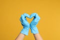 Doctor in medical gloves showing heart with hands on yellow background, closeup Royalty Free Stock Photo