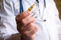 Doctor in medical lab coat holding pharmaceutical vials or ampoule of medicine, offering them patient on blurred background. Trea