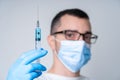 A doctor in a medical mask and gloves holds a syringe with a coronavirus vaccine and a vaccine chip inside. Conspiracy theory.