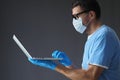 doctor in medical mask and gloves works in laptop