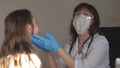 A doctor in medical mask with goggles and medical gloves examines throat and eyes of child. woman in white coat and Royalty Free Stock Photo