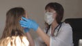 A doctor in medical mask with goggles and medical gloves examines throat and eyes of child. woman in white coat and Royalty Free Stock Photo