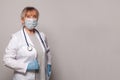 Doctor in medical mask, professional uniform coat, blue gloves and stethoscope standing on grey banner background. Royalty Free Stock Photo