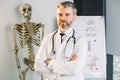 Doctor or medical professor with arms crossed and stethoscope around his neck looking at the camera, standing in modern Royalty Free Stock Photo