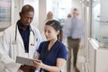 Doctor And Nurse Consulting Over Digital Tablet In Busy Hospital Corridor Royalty Free Stock Photo