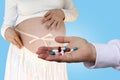 Doctor, nurse, pharmacist in white uniform holds out to a pregnant girl a handful of multi-colored pills, pharmacological concept Royalty Free Stock Photo