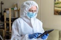 Doctor or nurse in PPE suit uses digital tablet in COVID-19 patient home Royalty Free Stock Photo