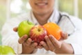 Doctor or nutritionist holding fresh fruit Orange, red and green apples and smile in clinic. Healthy diet Concept of nutrition f