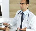 Doctor and patient discussing medical exam results while sitting at the desk in clinic. Male physician using tablet Royalty Free Stock Photo