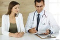 Doctor and patient discussing medical exam results while sitting at the desk in sunny clinic Royalty Free Stock Photo