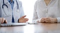 Doctor and patient discussing something while using laptop computer and sitting near each other at the wooden desk in Royalty Free Stock Photo