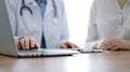 Doctor and patient discussing something while using laptop computer and sitting near each other at the wooden desk in Royalty Free Stock Photo