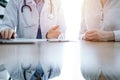 Doctor and patient discussing something while using laptop computer and sitting near each other at the wooden desk in Royalty Free Stock Photo