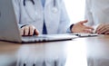 Doctor and patient discussing something while using laptop computer and sitting near each other at the wooden desk in Royalty Free Stock Photo