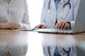 Doctor and patient discussing something while using laptop computer and sitting near each other at the wooden desk in Royalty Free Stock Photo