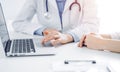 Doctor and patient sitting near each other at the desk in clinic. The focus is on female physician's hands using Royalty Free Stock Photo