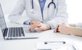 Doctor and patient sitting near each other at the desk in clinic. The focus is on female physician& x27;s hands using Royalty Free Stock Photo