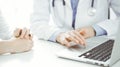 Doctor and patient sitting near each other at the desk in clinic. The focus is on female physician& x27;s hands using Royalty Free Stock Photo