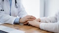 Doctor and patient sitting at the wooden table in clinic. Female physician& x27;s hands reassuring woman. Medicine